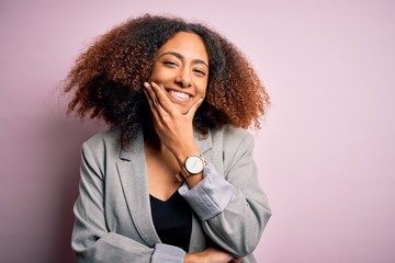 Young african american businesswoman with afro hair wearing elegant jacket looking confident at the camera smiling with crossed arms and hand raised on chin. Thinking positive.