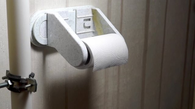 A hand tears pieces of toilet paper from a roll in toilet