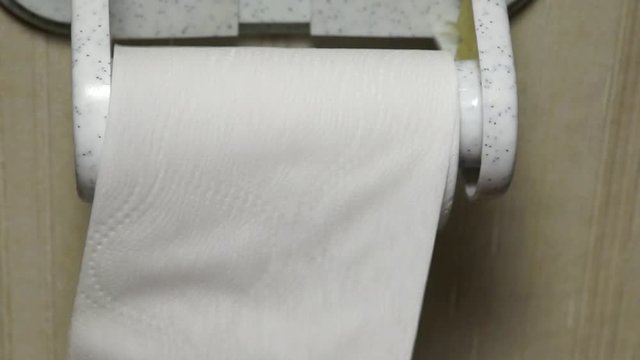 Hand tears pieces of toilet paper in toilet