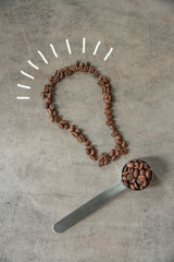 Coffee beans on metal spoon on a grey background. Coffee beans light bulb