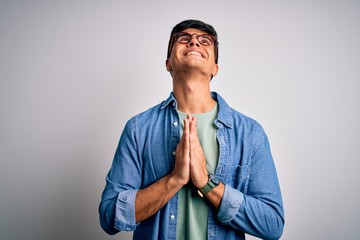 Young handsome man wearing casual shirt and glasses over isolated white background begging and...