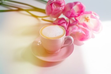 Still life with cup of cappuccino coffee and pink spring tulips flowers on white background. Pink design. Feminine. Home office, copy space