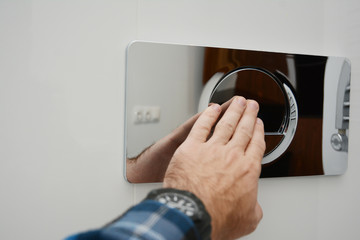 A man is pressing a wall-mounted polished chrome single flush plate to flush the toilet.