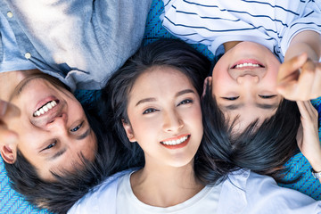 Asian family lying on sheet mat smiling face, looking at camera showing beautiful white teeth. Mother is in middle between father and kid. Strong white healthy teeth for dental care clinic concept.