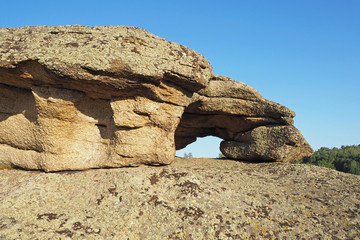 The fantastic stone arch on the big brown rock with spots of lichens, the clean blue sky