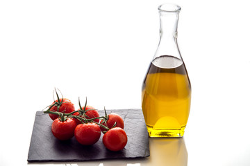 olive oil, bunch of tomatoes on slate and white background