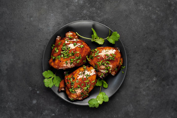 Grilled sweet chicken thighs with herbs and spices on a black plate on a stone background