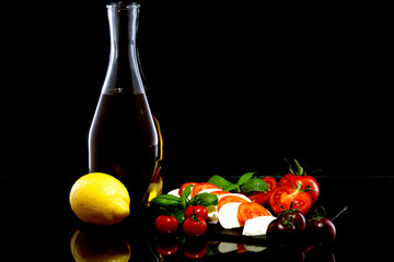 olive oil, tomatoes, basil, garlic, mozzarella and lemon on a black background