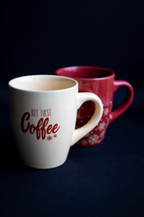Two red and beige coffee cups with lettering on dark black background