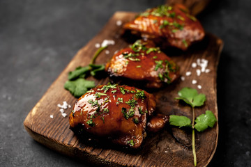 Grilled sweet chicken thighs on a cutting board on a stone background