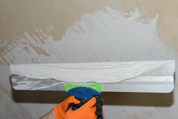 Puttying the wall with white plaster putty using a wide spatula
