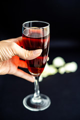Glass of red wine in a hand on dark black background