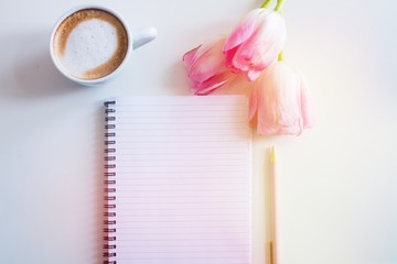 Empty notebook spring pink tulips flowers, cup of coffee. Mockup notepad on white background. Still life. Spring romantic mood. Colorful light. Top view. Copy space