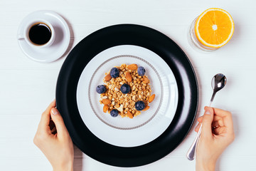 Woman's hand holding spoon near bowl of homemade granola