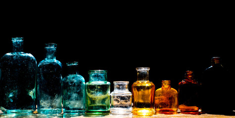 Colorful small glass bottles in sunlight on black background. Reflected light in the sun. Background glass. 