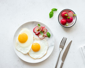 two fried eggs served with a salad of fresh radishes, basil and granular mustard above a light concrete background. Traditional breakfast food. top view. place for text