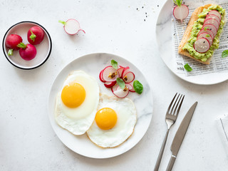 fried eggs with fresh radish salad and toast with mashed avocado, radish slices, sesame seeds and basil. healthy food concept. white concrete background. flat lay