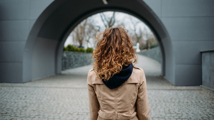 Rear view young woman with curly hair dressed in beige coat