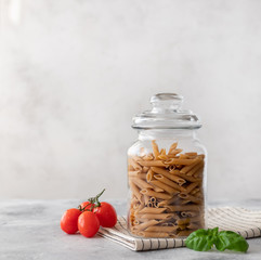 Wholewheat penne pasta in a glass container. close-up. diet concept. place for text. Gray...