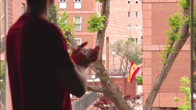 Joven aplaudiendo desde la ventana a los servicios m&eacute;dicos en Espa&ntilde;a en su lucha contra el COVID-19, foco en la bandera