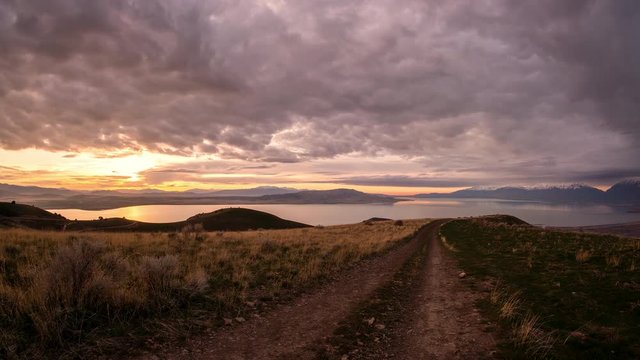 Looking down dirt road during sunset time lapse towards Utah Lake with super wide view on mountain top.