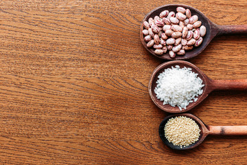 Obraz na płótnie Canvas White rice, pinto beans and proso millet seeds on wooden kitchen spoons.