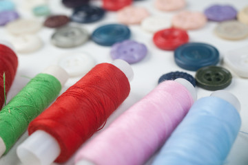 Multicolored buttons and threads are spread on white background