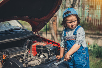 Little child trying to fix broken real car. Dreaming to be auto technician