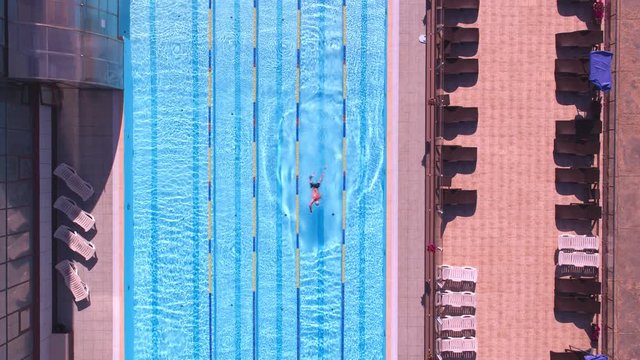 A lone swimmer in an Olympic outdoor pool is swimming in the early morning. Aerial shot with subject Tracking