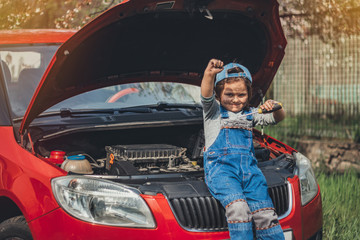 Little child trying to fix broken real car. Dreaming to be auto technician