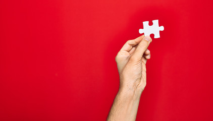 Beautiful hand of man holding piece of puzzle over isolated red background