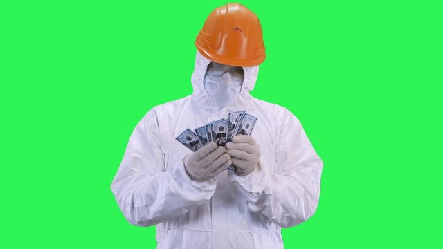 A man in a helmet and protective suit recounts money.Green screen background.