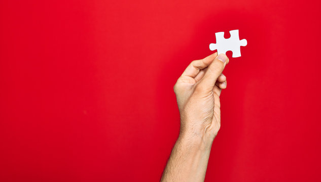 Beautiful hand of man holding piece of puzzle over isolated red background