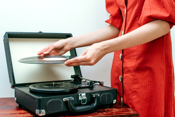 Young woman on retro dress playing vinyl record on turntable