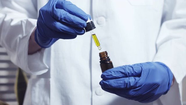 Examining cannabis cbd thc oil in medical scientist hands in pharmaceutical laboratory with mask and gloves. Closeup, 4k resolution