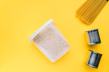 Food supplies crisis food stock for coronavirus quarantine isolation period in yellow background. different food in aluminum cans, Rice, pasta. Food delivery, Donation. top view. Copy space.