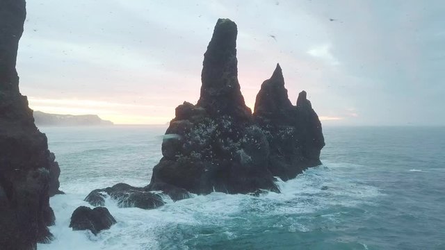 Reynisdrangar rocks at Reynisfjara Beach next to Vik i Myrdal at South Iceland.
Aerial drone shot flying over a cliff during sunrise.
Large storm waves crash rock.
High resolution footage. 4K