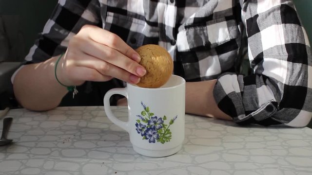 A pretty Girl dips oatmeal cookies into a mug of milk or cocoa. Breakfast.