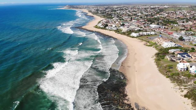 Aerial over ocean waves crashing over sandy shore of Jeffrey Bay in South Africa