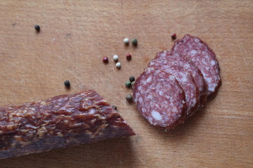 stick loaf smoked raw sausage and cut pieces of sausage peppers white black red on a wooden cutting Board