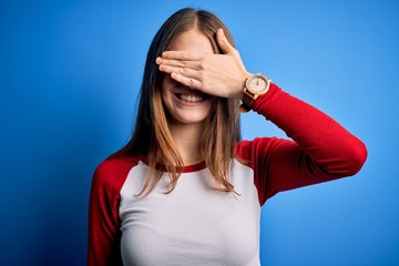 Fototapeta premium Young beautiful redhead woman wearing casual t-shirt over isolated blue background smiling and laughing with hand on face covering eyes for surprise. Blind concept.