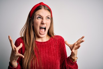 Young beautiful redhead woman wearing red casual sweater and diadem over yellow background crazy and mad shouting and yelling with aggressive expression and arms raised. Frustration concept.