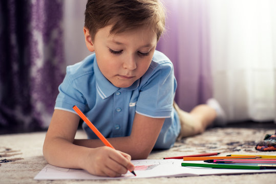 A happy child draws with pencils, lying on the floor of the house. Children's leisure. Family and children.