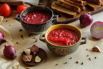 Soup borscht on a beige background in a clay plate with garlic, onion, pepper, sour cream and bread