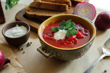 Soup borscht on a beige background in a clay plate with garlic, onion, pepper, sour cream and bread