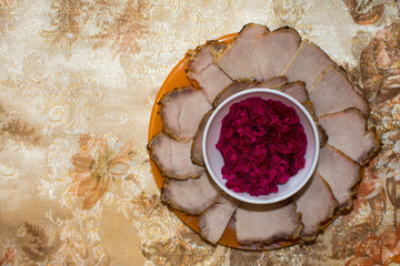 Ukrainian traditional Easter food - slices of baked meat and special sauce of blended boiled beet with horseradish on a white plate. Selective focus. Copy space.
