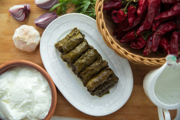Delicious dolma sarma rice, white yogurt sauce . Garlic, red onion, tarragon . In a stuffed white plate . Yogurt and dried beans in a brown bowl . Red Dry Pepper in Traditional Basket .