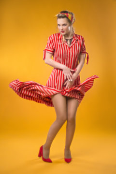 Pin-up girl in a striped dress. Classic soft focus. Flying hem of the dress. On a yellow background
