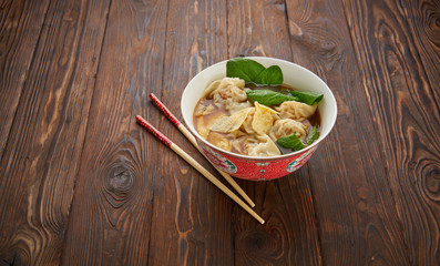 Homemade asian wonton dumpling soup in traditional red chinese bowl with wooden chopsticks over wooden texture background. Top view flat lay, copy space asia food concept