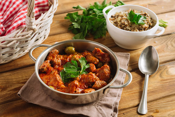 Beef goulash in tomato sauce with olives and boiled buckwheat. Served with fresh parsley leaves. Homemade food. Wooden table. Rustic style.